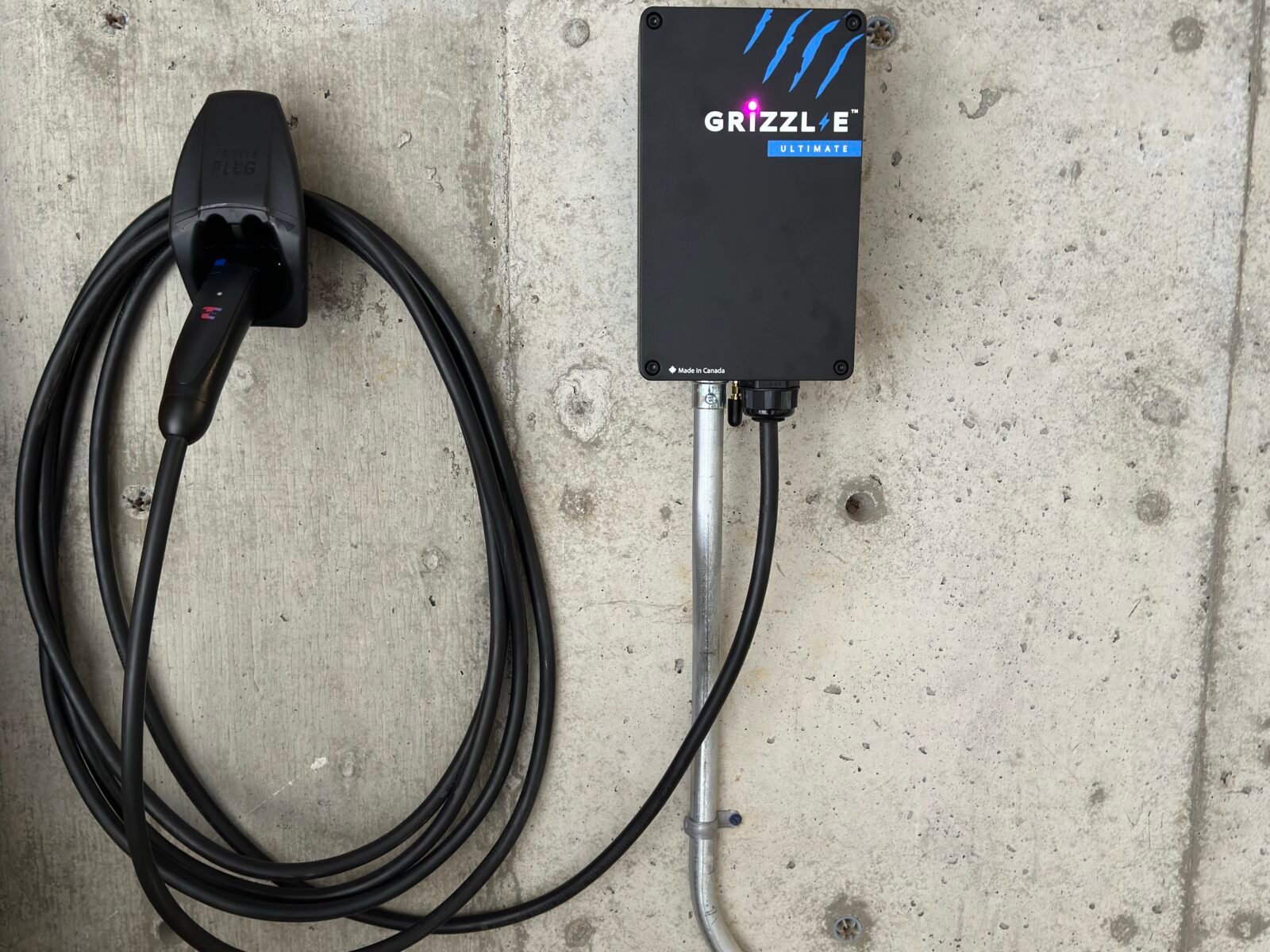 Wall-mounted Grizzl-E EV charger with conduit and coiled charging cable on a concrete garage wall